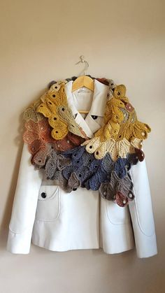 a white jacket with multicolored crochet and buttons on the collar is hanging up against a wall