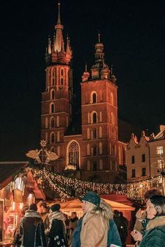 people are walking around in front of an old building with christmas lights on the outside