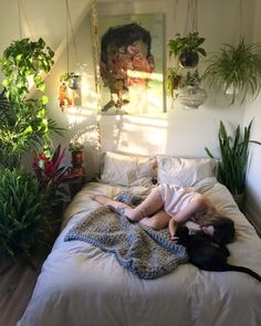 a woman laying on top of a bed under a blanket next to potted plants