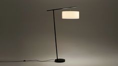 a floor lamp with a white shade on the top and black base, in front of a gray background