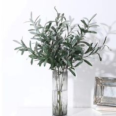 a glass vase filled with green leaves on top of a white table next to a mirror