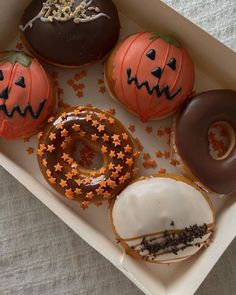 four decorated doughnuts in a box with sprinkles and jack - o'- lanterns