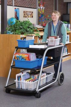 a woman standing next to a cart filled with books and magazines in an office setting