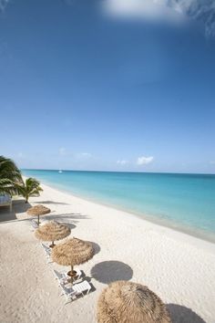 beach chairs and umbrellas are lined up on the white sand near the blue water