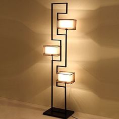 a lamp that is sitting on top of a floor next to a wall with four square lights