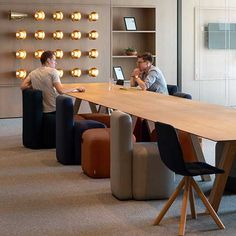 two people sitting at a table with laptops on it in the middle of an office