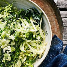 a white bowl filled with green vegetables on top of a wooden table next to a blue towel