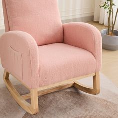 a pink rocking chair sitting on top of a rug in front of a potted plant