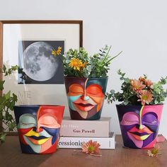 three planters with different faces on them sitting on a table next to a framed photograph