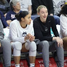 two female basketball players are sitting on the bench and one is talking to another player