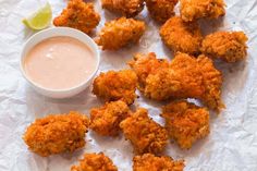 fried food with dipping sauce on white paper next to small bowl and lime wedges