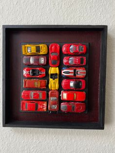 there are many toy cars in a shadow box on the wall and one is red