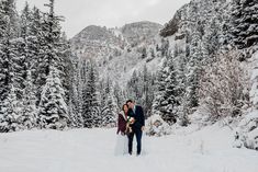 a bride and groom kissing in the snow surrounded by pine trees on their wedding day