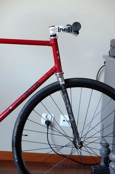 a close up of a red bike on a wooden floor with a white wall in the background