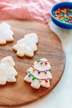 cookies decorated with christmas trees on a wooden platter next to a bowl of candy