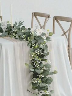 the table is set with white linens and greenery on it, along with candles