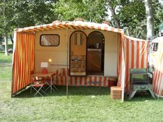 an orange and white striped tent sitting on top of a grass covered field next to trees