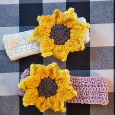 three crocheted flower headbands on a checkered tablecloth with one sunflower in the center