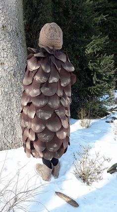 a person standing in the snow next to a large pine cone shaped tree trunk that has leaves on it