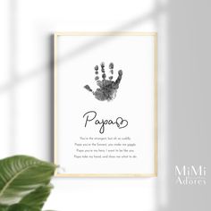 a framed print with the words papao and handprints on it, next to a potted plant