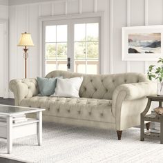 a living room filled with furniture and a coffee table on top of a rug in front of two windows