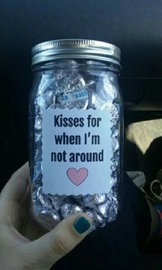 a person holding up a jar with candy in it that says kisses for when i'm not around