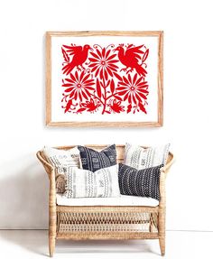 a red and white painting hanging on the wall above a wicker chair with pillows