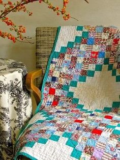 a chair with a quilt on it next to a table and tree branch in the background