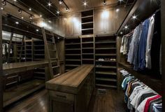 a walk in closet with wooden shelves and lights on the ceiling, along with hanging clothes