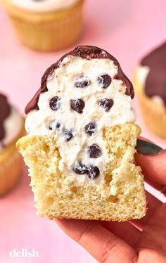 a hand holding a half eaten cupcake with white frosting and chocolate chips