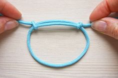 two hands holding a blue string bracelet