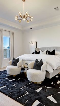 a bedroom with a large bed and two chairs in front of the window, along with a chandelier