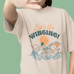 Step back in time with our retro-inspired wing foiling tee, featuring a hand-drawn wing foil illustration. With our wingfoildaily slogan 'Let's Go Winging!', this vintage-inspired shirt is a must-have for any beach enthusiast. Get ready to make waves and memories with this vintage sports shirt that screams style and adventure. Highlights: Medium fabric (5.3 oz/yd² or 180 g/m²) Classic fit True to size 100% cotton Unisex Perfect as a gift or to add to your collection of surfing gifts, embrace the Crew Neck T-shirt With Front Print For Surfing, Surfing Graphic Tee With Screen Print, Graphic Surfing T-shirt With Screen Print, Surfing Graphic Tee With Crew Neck, Surfing Graphic Print Crew Neck T-shirt, Graphic Tee With Screen Print For Surfing, Graphic Tee T-shirt With Front Print For Surfing, Surfing Graphic Print Relaxed Fit T-shirt, Graphic Print Crew Neck T-shirt For Surfing