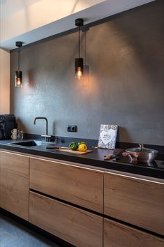 a modern kitchen with black counter tops and wooden cabinets, along with hanging lights above the sink