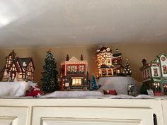 a shelf filled with christmas decorations on top of a white cupboard under a light fixture