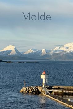 a lighthouse sitting on top of a pier next to the ocean with snow covered mountains in the background