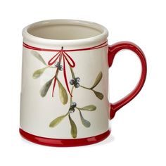 a red and white coffee mug with green leaves on it's rim, decorated with holly berries