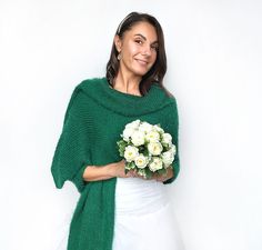 a woman wearing a green shawl holding a bouquet of white flowers in her hands