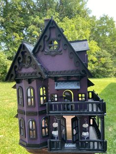 a purple doll house sitting on top of a wooden table in the grass next to trees