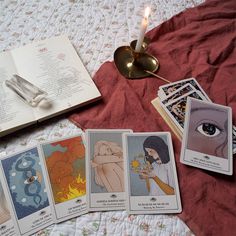 an open book and some cards on a bed next to a lit candle with candles