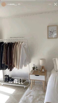 a bedroom with white walls and clothes hanging on the rack