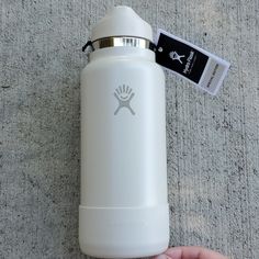 a hand holding a white water bottle next to a tag on the ground with a black and white sticker