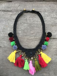 "This wax-cotton macrame braided necklace is covered in tigers eye crystals, brass and brightly colored tassels. The festive necklace is braided with beads and stones using wax string and made by Hmong Hill Tribe artisans in Northern Thailand. The necklace is 17\" long with two size loops and brass bead closure. The main design measures 5\" high and 4\" wide." Traditional Macrame Necklaces For Festivals, Multicolor Macrame Necklace For Festivals, Artisan Multicolor Macrame Jewelry, Bohemian Multicolor Macrame Necklaces, Bohemian Black Hand Knotted Jewelry, Bohemian Black Macrame Necklace, Hippie Style Multicolor Macrame Jewelry, Bohemian Multicolor Macrame Necklace, Black Woven Jewelry For Festivals