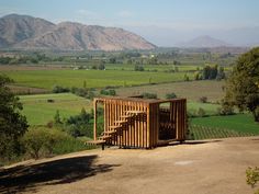 a wooden structure sitting on top of a dirt field next to trees and mountains in the background