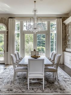 a dining room table with chairs and chandelier in front of two large windows