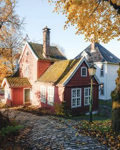 a red house with white windows and a brick walkway leading to the front door is surrounded by autumn foliage