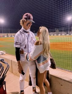 a man and woman in baseball uniforms standing next to each other on a field at night