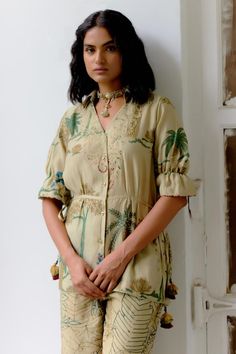 Sage ivory shirt with hand painted floral kalamkari patterns and applique detailing on yoke. Comes with tropical kalamkari pattern pant.
Components: 2
Pattern: Hand Painted
Type Of Work: Kalamkari
Neckline: V Neck
Sleeve Type: Elbow
Fabric: Hand Spun Cotton
Color: Beige
Other Details: 
Adjustable side tie-up shirt
Top length: 29 inches
Disclaimer: Pure hand painted kalamkari pieces will have irregularities, no pieces will be identical
Occasion: Work - Aza Fashions Bohemian Designer Top For Summer, Tropical Pants, Tie Up Shirt, Cotton Painting, Up Shirt, Pants Pattern, Hand Spinning, Aza Fashion, Pants Set