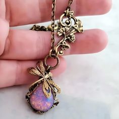 Dragonfly necklace with vintage Czech glass fire opal jewel; Art Nouveau era Lalique style inspiration.  The stone has a milky pink opal sheen that glows bright, as if on fire, when light hits it.  Size Adjustable for a perfect fit, choose your necklace length upon checkout.  Pendant including the hoop is 1.25"L (3.1 cm) Finish: Antique gold-tone patina on solid brass. Stone: Glass fire opal cabochon is new unused limited vintage stock made in Czechoslovakia.   * All metal components are high quality solid brass, lead and nickel free. * Great gift for any occasion; Arrives ready to gift in a beautiful gift box. * Signed with my original hand engraved logo. Limited Availability: Each piece is handcrafted and unique, available in limited quantities, and exclusively sold by Eras Jewelry -  In Vintage Opal Gemstone Jewelry, Pink Opal Pendant Necklace As A Gift, Handmade Mystical Opal Necklaces, Handmade Mystical Opal Necklace, Opal Cabochon Necklaces, Handmade Vintage Opal Jewelry, Nickel-free Opal Necklaces As Gift, Nickel-free Opal Necklace Gift, Handmade Pink Opal Pendant Necklace