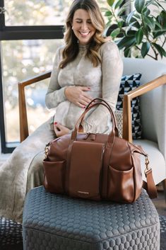 a woman sitting in a chair with a brown purse on top of her lap and smiling